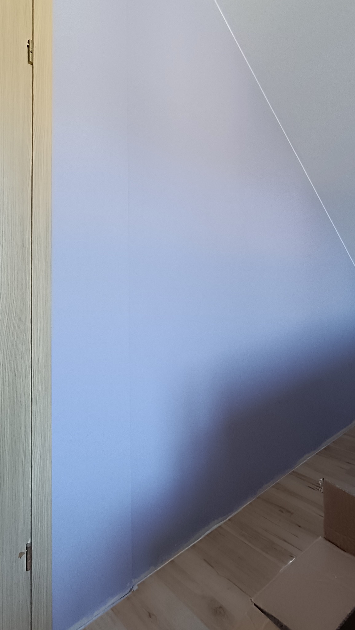 Ściana w odcieniach fioletu po malowaniu, widoczny fragment podłogi z panelami i narożnik szafy z jasnego drewna. Ukośny sufit w tle.