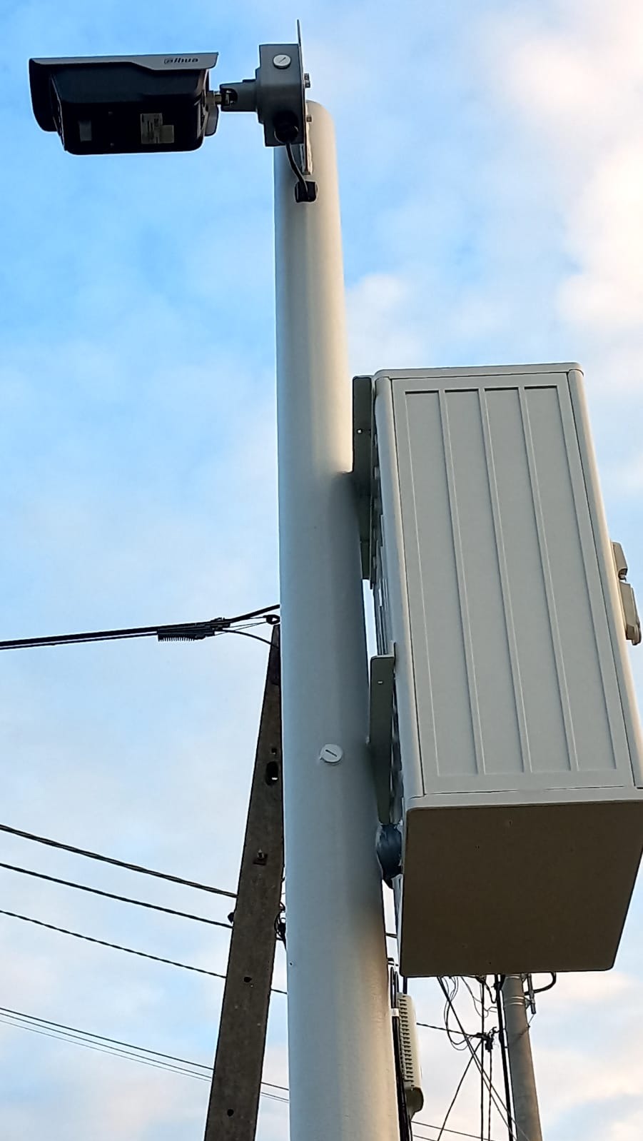 Kamera monitoringu Dahua na słupie z puszką elektryczną, skierowana w górę na błękitne niebo. Widoczne przewody i słup energetyczny w tle.