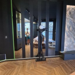 Remonty Wojciech - Nowoczesne wykończenie wnętrza w Lublinie: parkiet ułożony w jodełkę, czarne ściany i lustra z podświetleniem LED. Widoczna rzeźba i odbicie osoby.