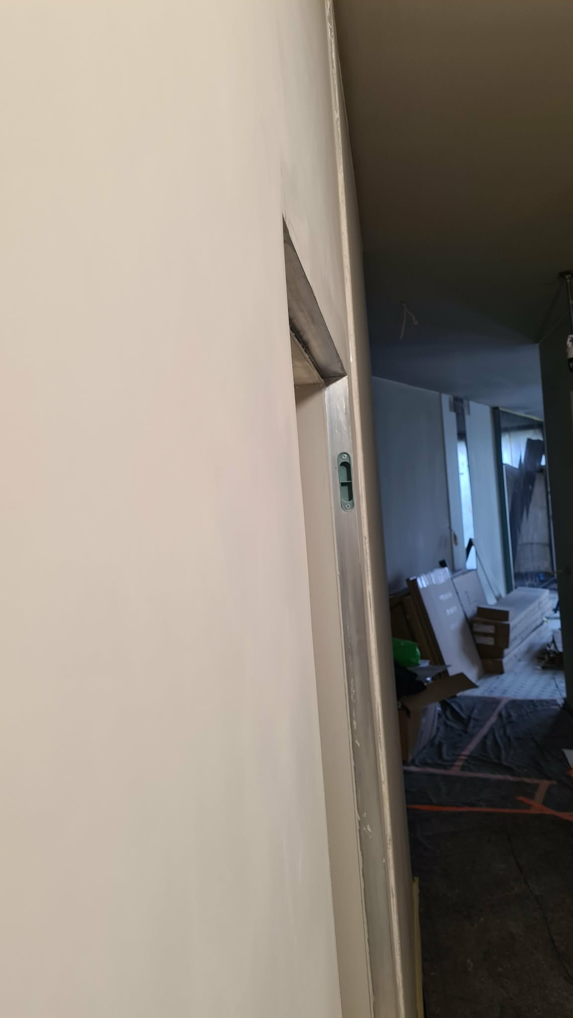 Świeżo wyszpachlowana ściana z widoczną ościeżnicą i fragmentem wnętrza w tle, ukazująca gładką powierzchnię przygotowaną do malowania.