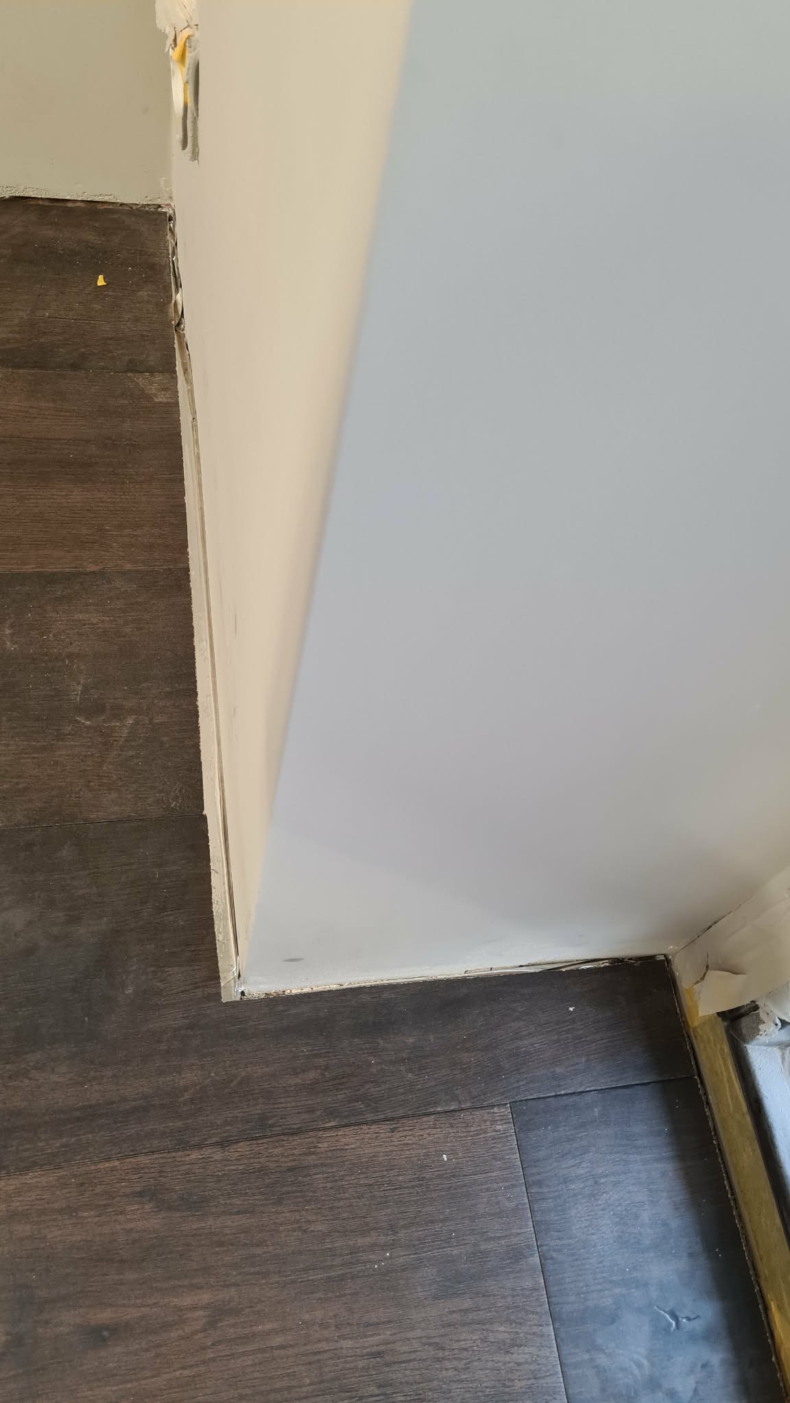 Fragment wykończonego wnętrza: ciemna podłoga z paneli, świeżo pomalowana ściana w jasnym odcieniu, widoczne łączenie podłogi ze ścianą. Detal wykończenia.
