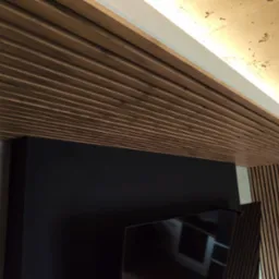 Drewniany sufit lamelowy z oświetleniem LED, czarna ściana pod telewizor i dekoracyjna szara ściana. Nowoczesne wykończenie wnętrza z dbałością o detale.