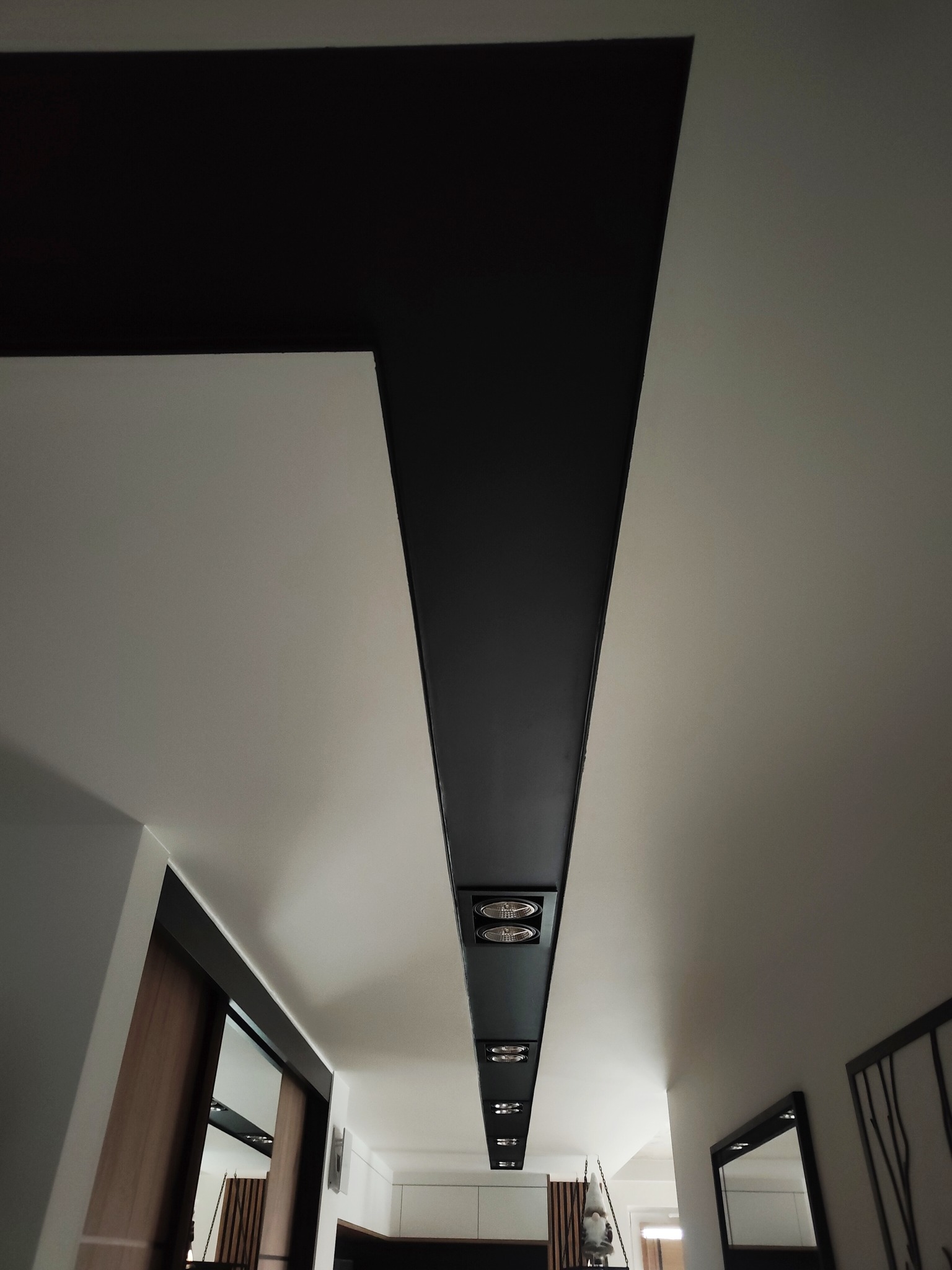 Nowoczesny sufit w mieszkaniu z podłużnym, czarnym pasem oświetleniowym i białymi ścianami. Minimalistyczny design wnętrza.