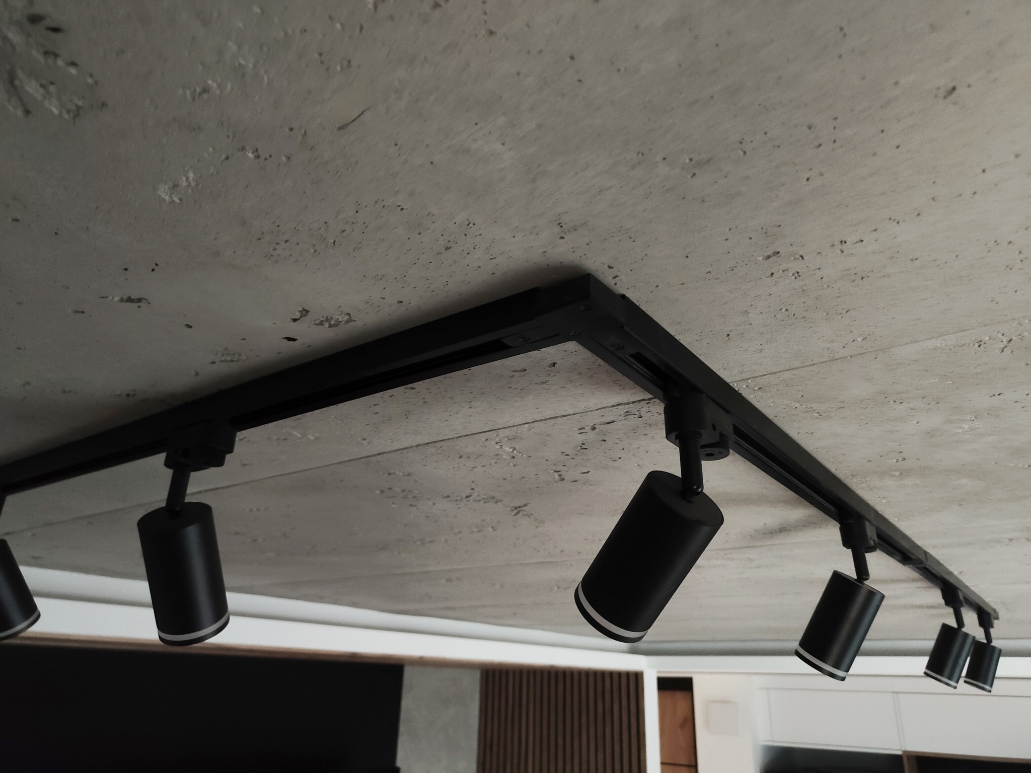 Betonowy sufit z zamontowanym czarnym systemem szynowym oświetlenia punktowego. Minimalistyczny design wnętrza.