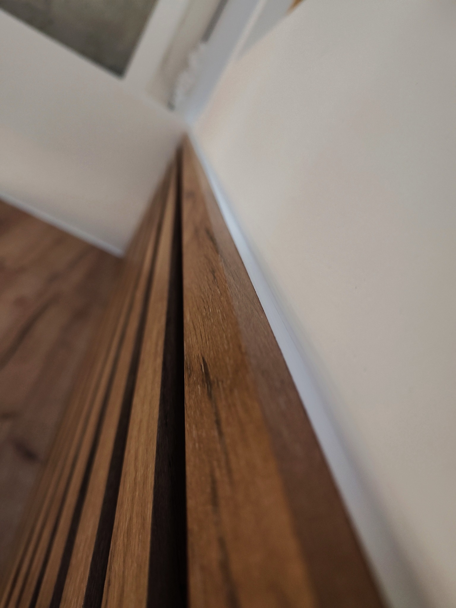 Detal wykończenia wnętrza: brązowe, drewniane panele ścienne zamontowane na styku z białą ścianą i sufitem. Ujęcie z dołu podkreśla pionowe linie paneli.