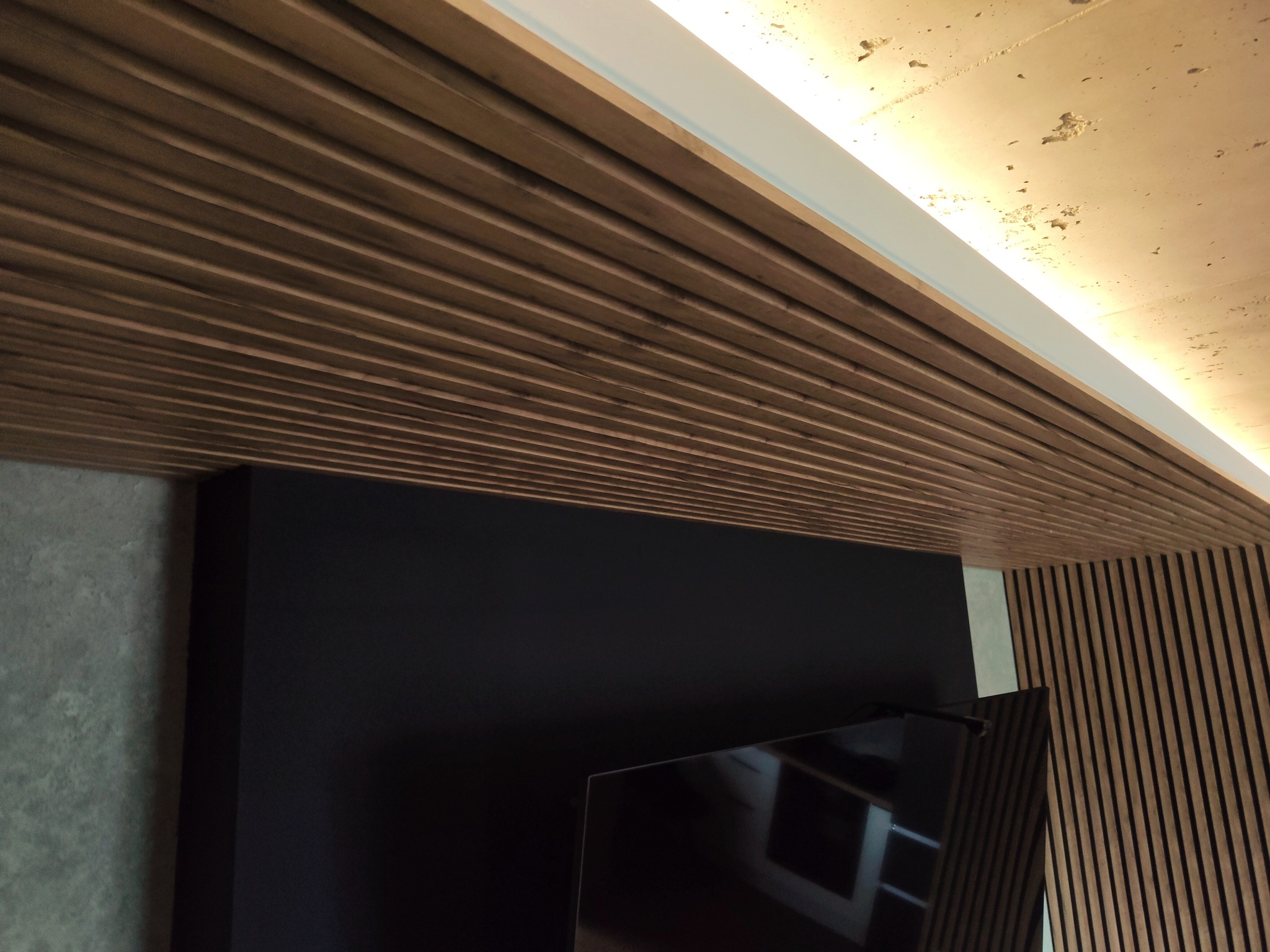 Drewniany sufit lamelowy z oświetleniem LED, czarna ściana pod telewizor i dekoracyjna szara ściana. Nowoczesne wykończenie wnętrza z dbałością o detale.