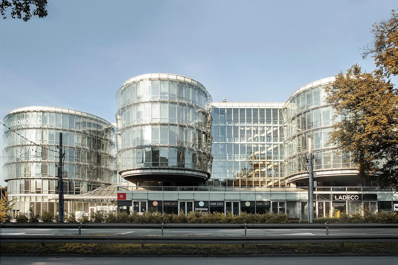 Szklany biurowiec Pomorskiego Parku Naukowo-Technologicznego w Gdyni, z widocznymi lokalami usługowymi na parterze, w słoneczny dzień.