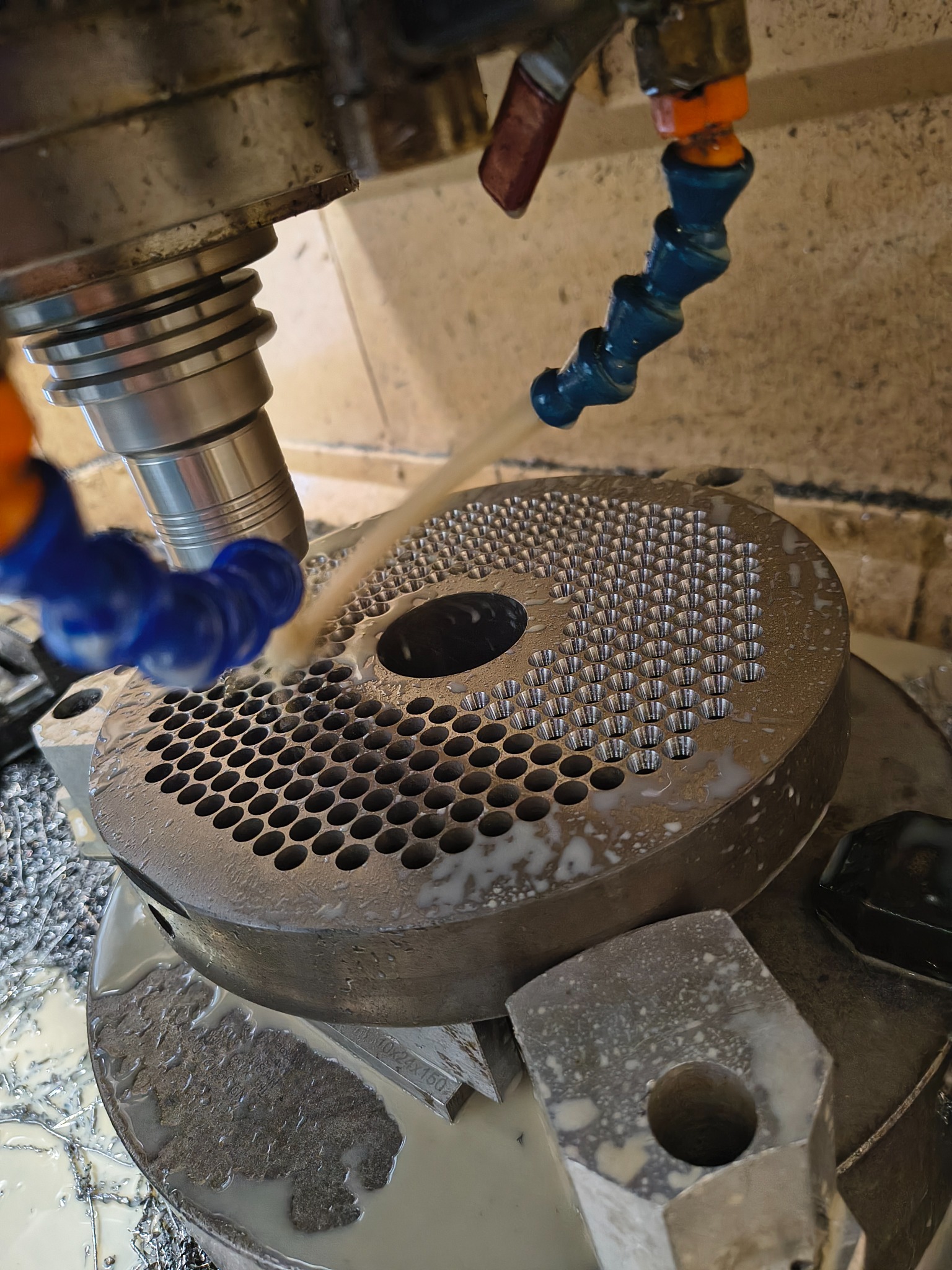 Frezowanie CNC metalowego elementu z licznymi otworami, chłodzonego cieczą. Widoczne wióry i narzędzie obróbcze.