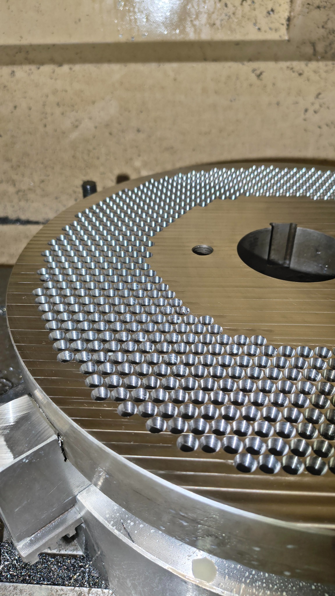 Metalowy dysk z rzędami precyzyjnie wywierconych otworów, widoczne ślady obróbki, surowy detal po procesie wiercenia, jasne oświetlenie.