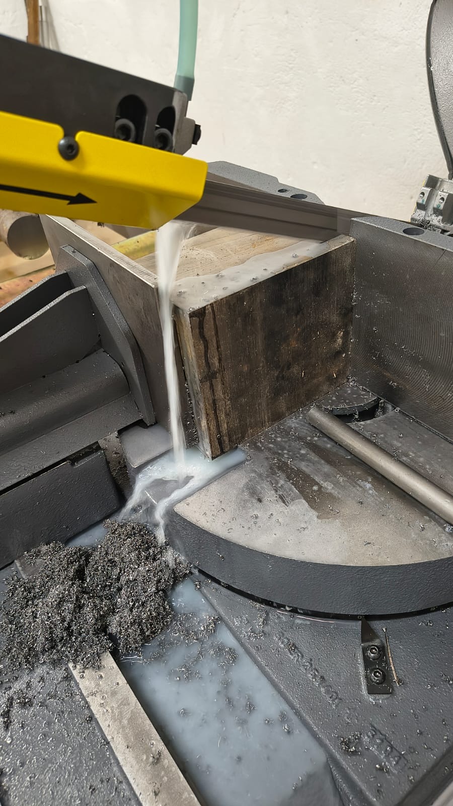 Cięcie metalowego bloku piłą taśmową z chłodziwem, widoczne wióry i narzędzie. Proces obróbki metalu w warsztacie ślusarskim.