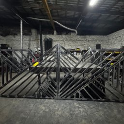 Loft Weld - Surowe, metalowe dwuskrzydłowe ogrodzenie z ukośnymi prętami w warsztacie. Widoczne ślady spawania i obróbki. W tle narzędzia i wyposażenie warsztatowe.