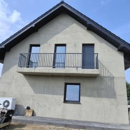 Loft Weld - Nowoczesny dom z balkonem zabezpieczonym prostą, metalową balustradą w kolorze grafitowym. W tle błękitne niebo i fragmenty innych budynków.