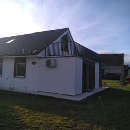 Loft Weld - Nowoczesny dom z balkonem zabezpieczonym czarną, metalową balustradą. Widok z ogrodu, w tle błękitne niebo i sąsiednie budynki. Minimalistyczny design.