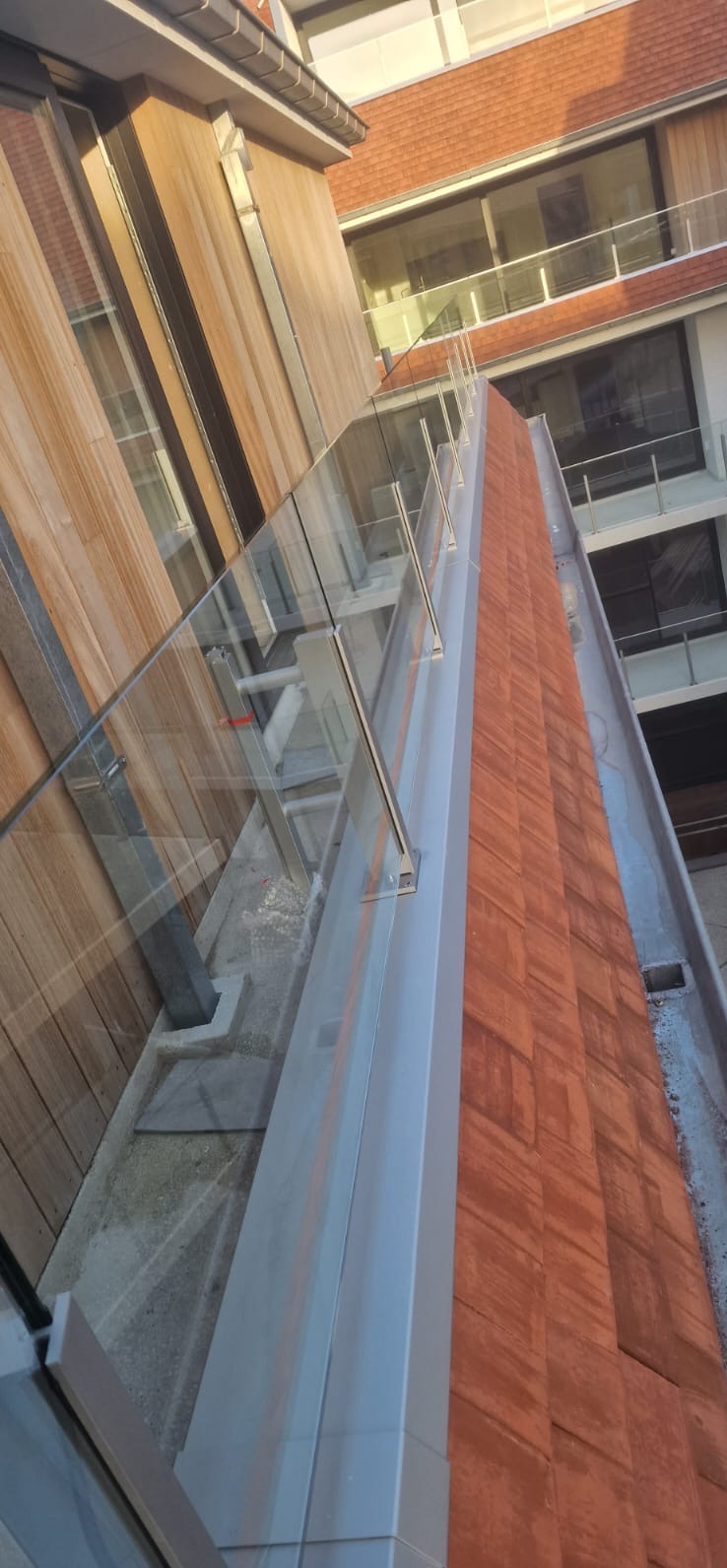 Nowoczesna balustrada szklana z elementami ze stali nierdzewnej zamontowana na balkonie budynku. Widok z dołu, podkreślający detale mocowań i przejrzystość szkła.