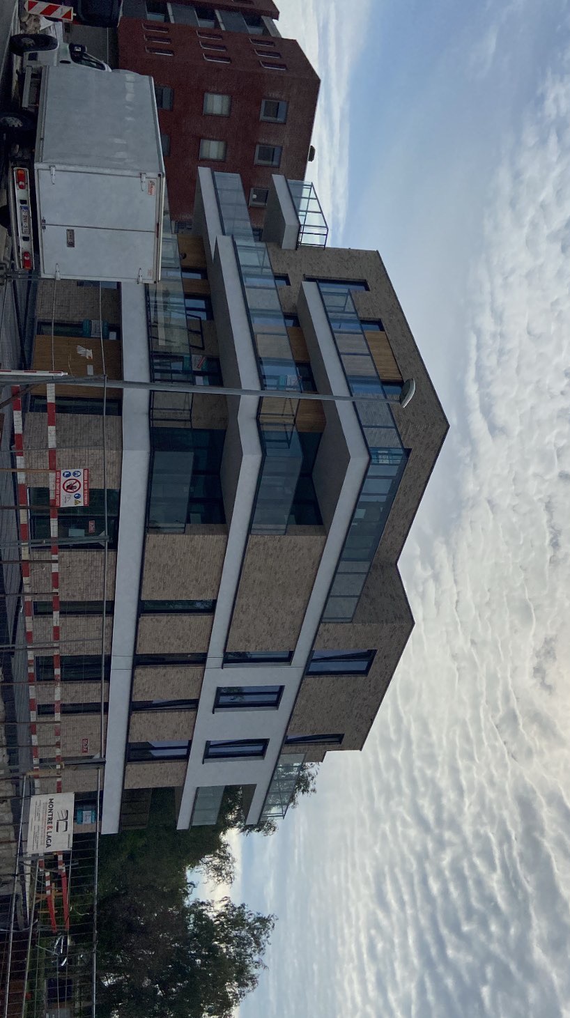 Nowoczesny budynek z balkonami ze szkła, widoczny z dołu, z fragmentem ciężarówki i rusztowań. Nietypowe chmury na niebie.