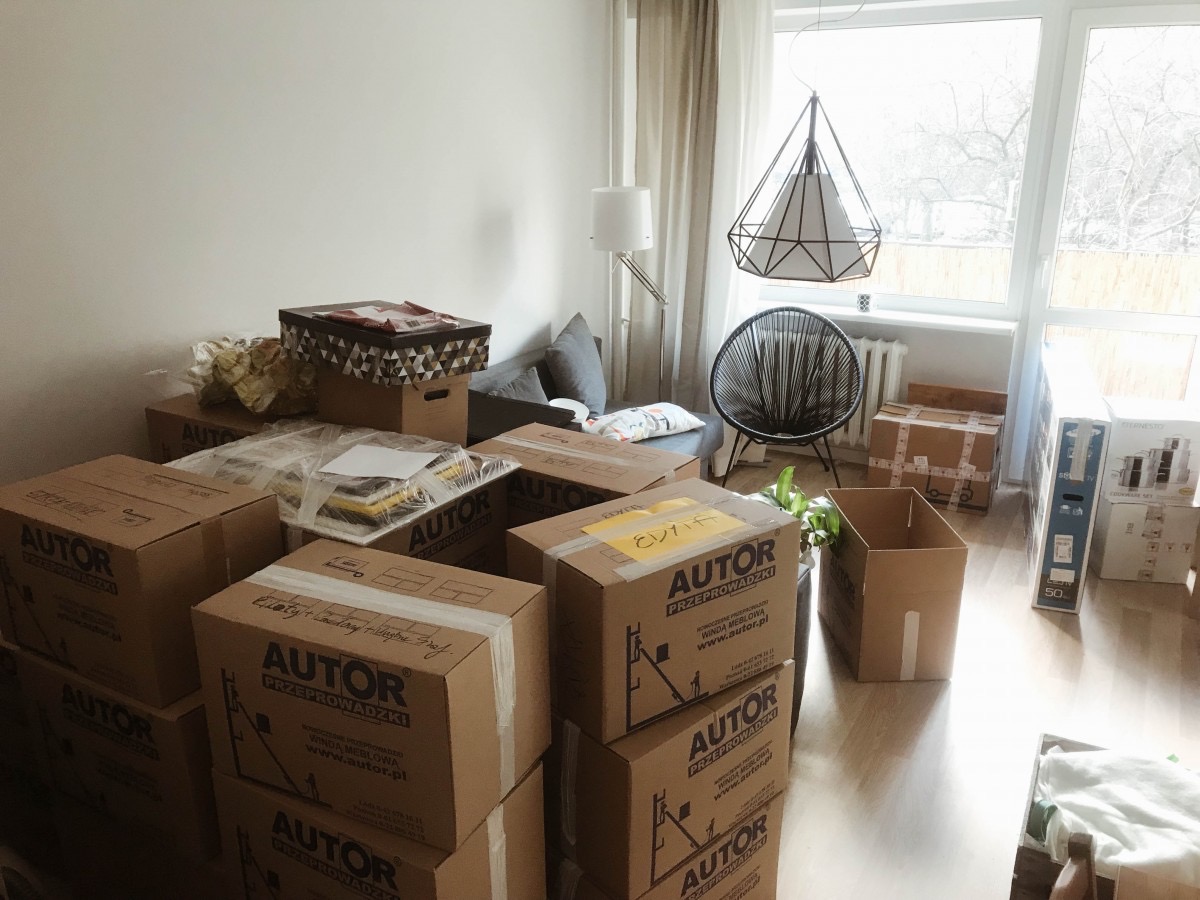 Pokoje wypełnione kartonami firmy przeprowadzkowej AUTOR z Krakowa. Widoczne meble i okno. Kartony podpisane, gotowe do transportu. Jasne wnętrze.