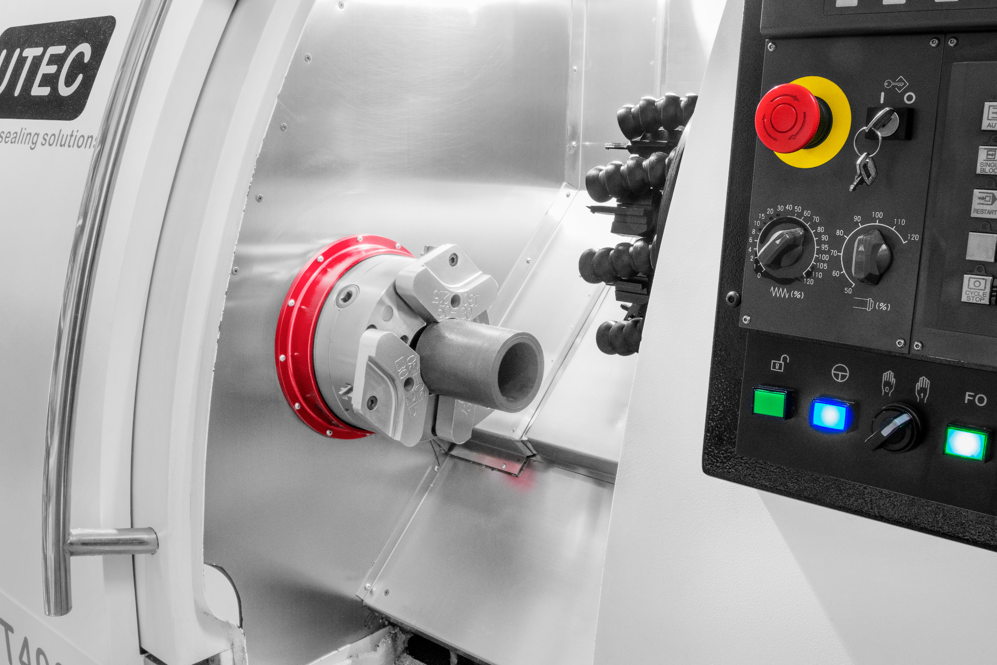Precyzyjna tokarka CNC UTEC z uchwytem i zamocowanym elementem. Panel sterowania z przyciskami i pokrętłami. Widoczne uszczelnienia i detale maszyny.