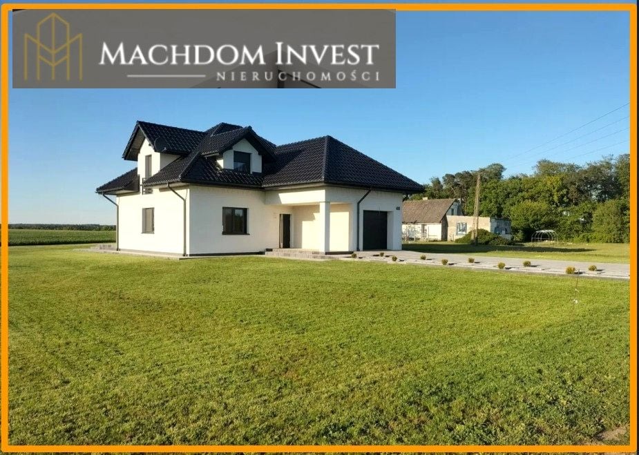 Nowoczesny, parterowy dom z garażem i czarnym dachem na dużej działce z równo przystrzyżonym trawnikiem. W tle widoczny budynek gospodarczy.