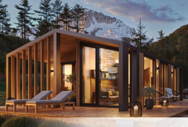 Nowoczesny, parterowy dom modułowy z dużymi przeszkleniami, otoczony lasem i górami w tle. Dwa leżaki na tarasie zachęcają do relaksu.