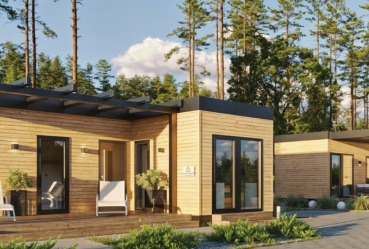 Nowoczesny, parterowy dom modułowy z drewnianą elewacją, czarną stolarką i zadaszeniem. Z przodu taras z białym krzesłem i roślinami. W tle las iglasty.