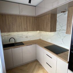 ProMebelek - Jasna kuchnia w stylu skandynawskim: białe fronty dolne, drewnopodobne górne szafki, marmurowy backsplash, czarna armatura i oświetlenie punktowe.