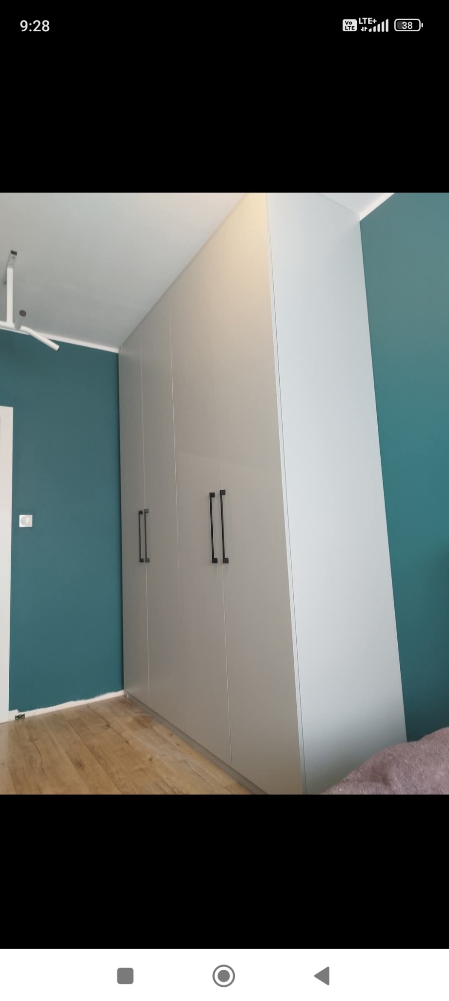 Elegancka, jasnoszara szafa wnękowa z czarnymi uchwytami na tle turkusowej ściany i drewnianej podłogi. Minimalistyczny design, nowoczesne oświetlenie.