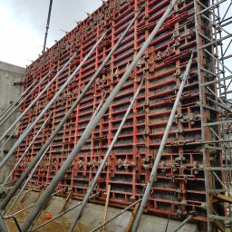 Adrian Ducki Przedsiębiorstwo Usług Budowlanych - Szczegółowe ujęcie szalunku zbrojeniowego, wspartego metalowymi stemplami, przygotowanego do zalewania betonem. Widoczne elementy konstrukcyjne i mokre podłoże.