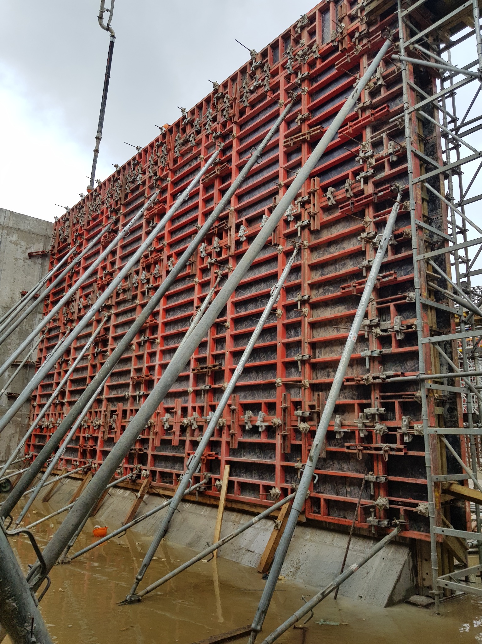 Szczegółowe ujęcie szalunku zbrojeniowego, wspartego metalowymi stemplami, przygotowanego do zalewania betonem. Widoczne elementy konstrukcyjne i mokre podłoże.