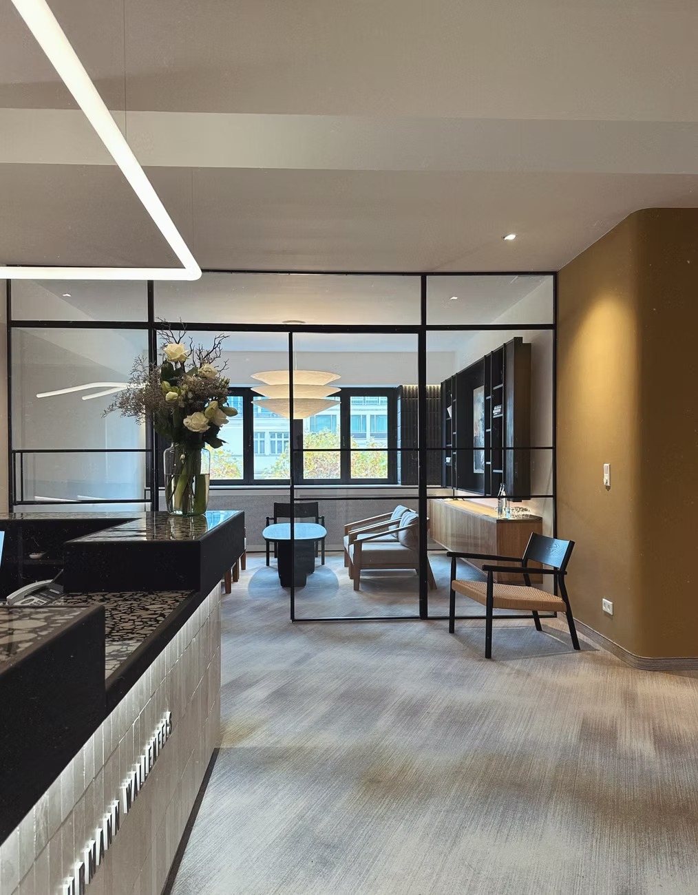 Eleganckie wnętrze biura z przeszkloną ścianą działową, nowoczesnym oświetleniem, minimalistycznym wystrojem i blatem recepcyjnym z dekoracyjnym wykończeniem.