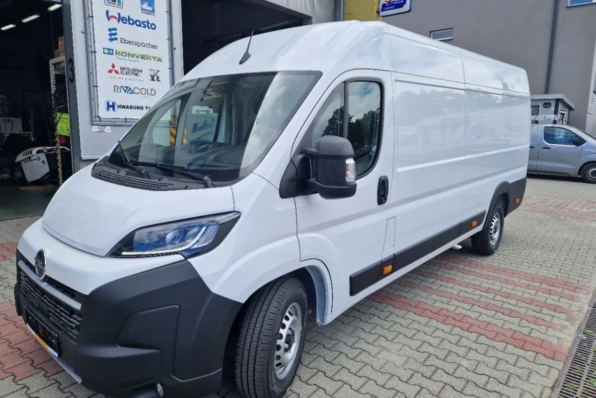 Biały bus dostawczy marki Fiat Ducato, zaparkowany na zewnątrz budynku, widok z przodu i boku, na tle szyldu z logo firm chłodniczych.