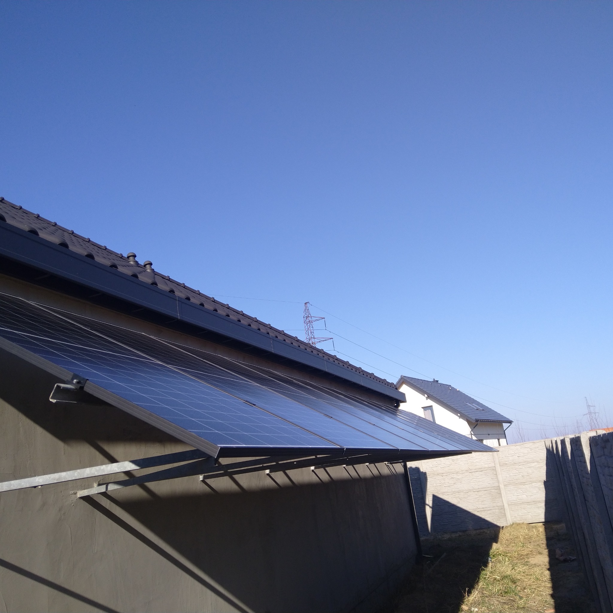 Panele słoneczne zamontowane na dachu domu jednorodzinnego, widoczne elementy konstrukcyjne, błękitne niebo w tle. Nowoczesna instalacja fotowoltaiczna.