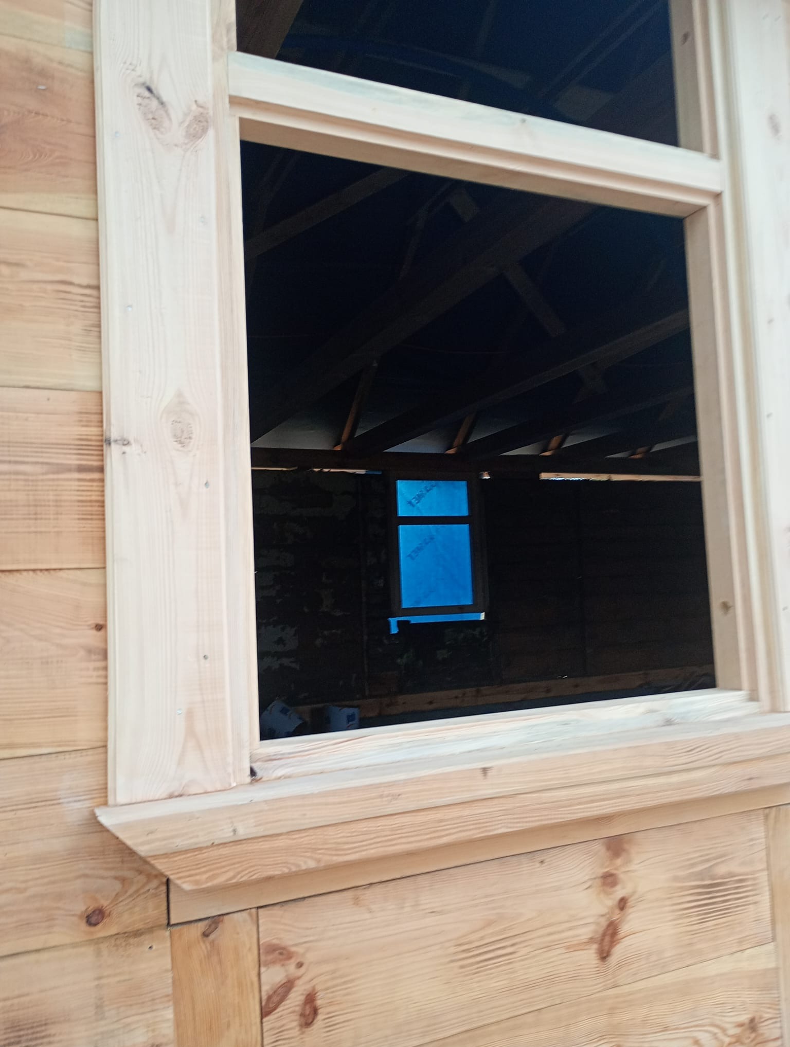 Surowe drewno: rama okienna z widocznym wnętrzem budynku w trakcie budowy. Detal sęków i usłojenia drewna. Ujęcie z dołu, podkreślające solidność konstrukcji.