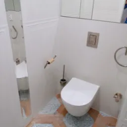 Nowoczesna, biała toaleta podwieszana w wykończonej łazience. Dekoracyjne, heksagonalne płytki podłogowe w odcieniach błękitu i drewna. Widok na lustro i wyposażenie.