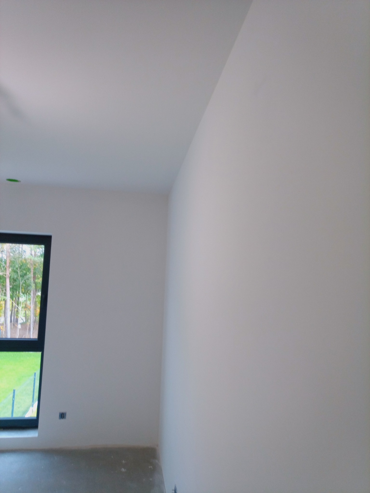 Jasne wnętrze po malowaniu: białe ściany, czarna rama okna z widokiem na zieleń. Gładkie powierzchnie, świeżo pomalowane, minimalistyczny styl. Nowoczesne wykończenie.