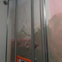 Stelaż z profili metalowych przy ścianie z instalacją elektryczną, przygotowany do zabudowy, widoczne elementy mocujące i fragment drabiny.