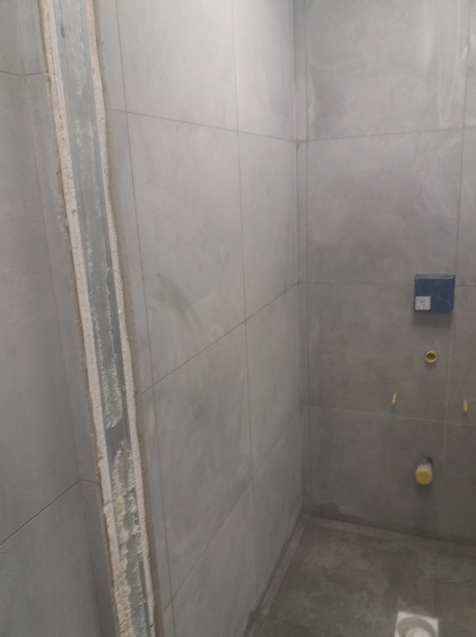 Wnętrze łazienki w Ciechanowie w trakcie remontu. Widoczne szare płytki ścienne, zamontowany stelaż podtynkowy i odpływ liniowy w podłodze.