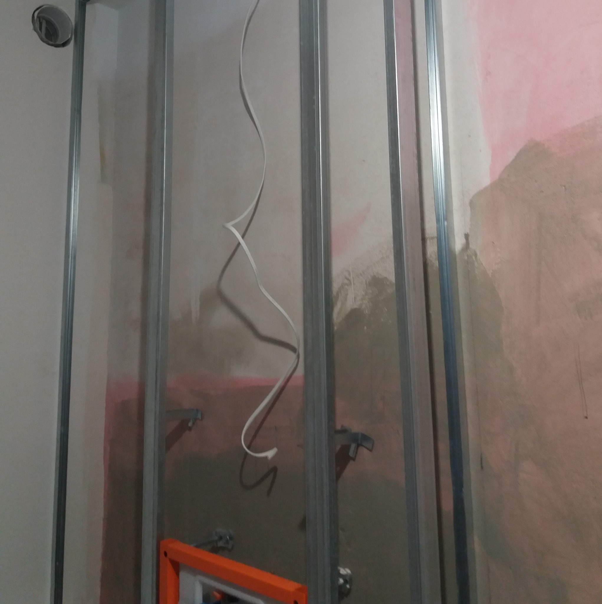 Stelaż z profili metalowych przy ścianie z instalacją elektryczną, przygotowany do zabudowy, widoczne elementy mocujące i fragment drabiny.