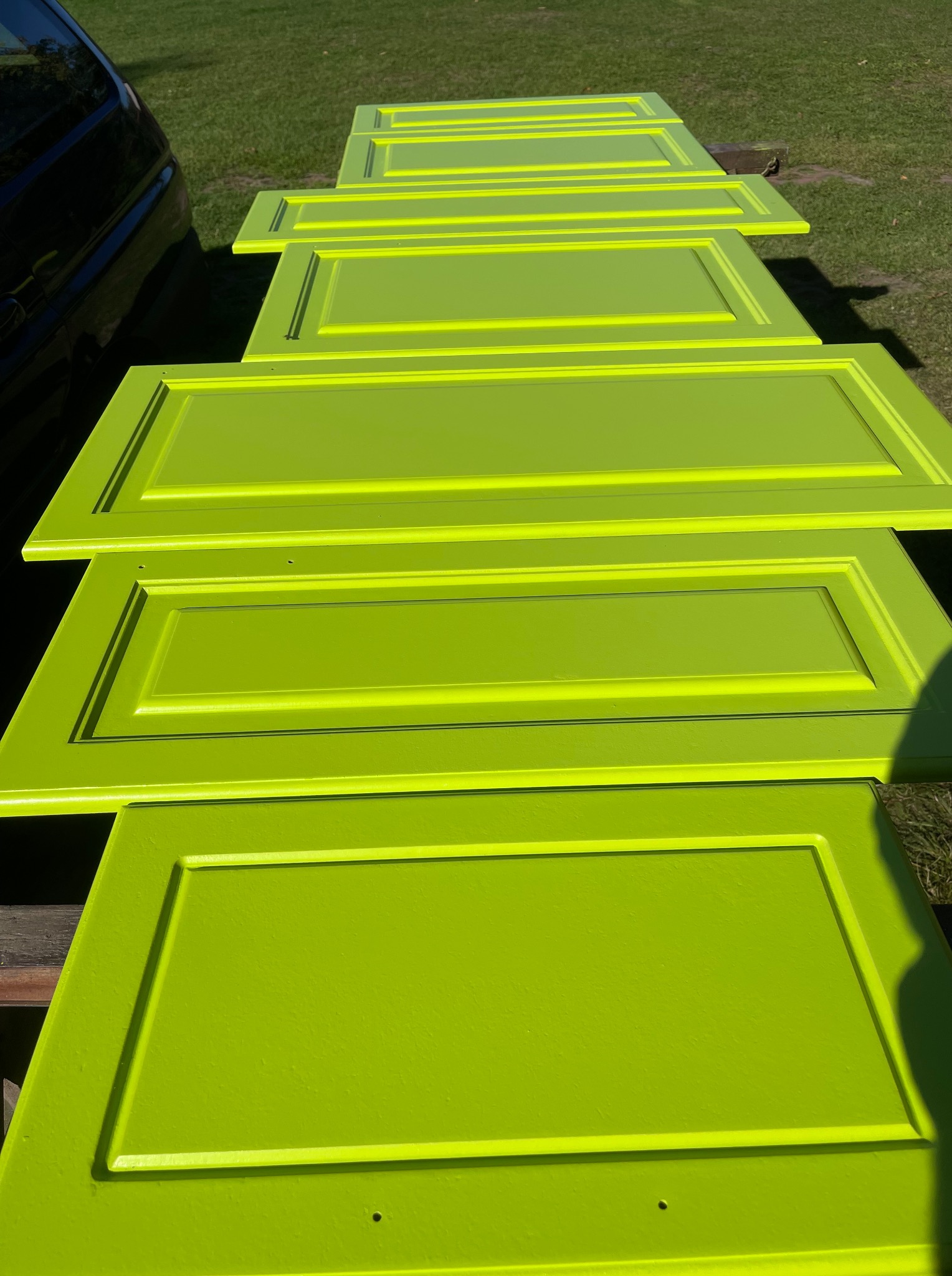 Świeżo pomalowane na jaskrawy, limonkowy kolor fronty szafek kuchennych, ułożone rzędem na zewnątrz w słoneczny dzień, gotowe do montażu.