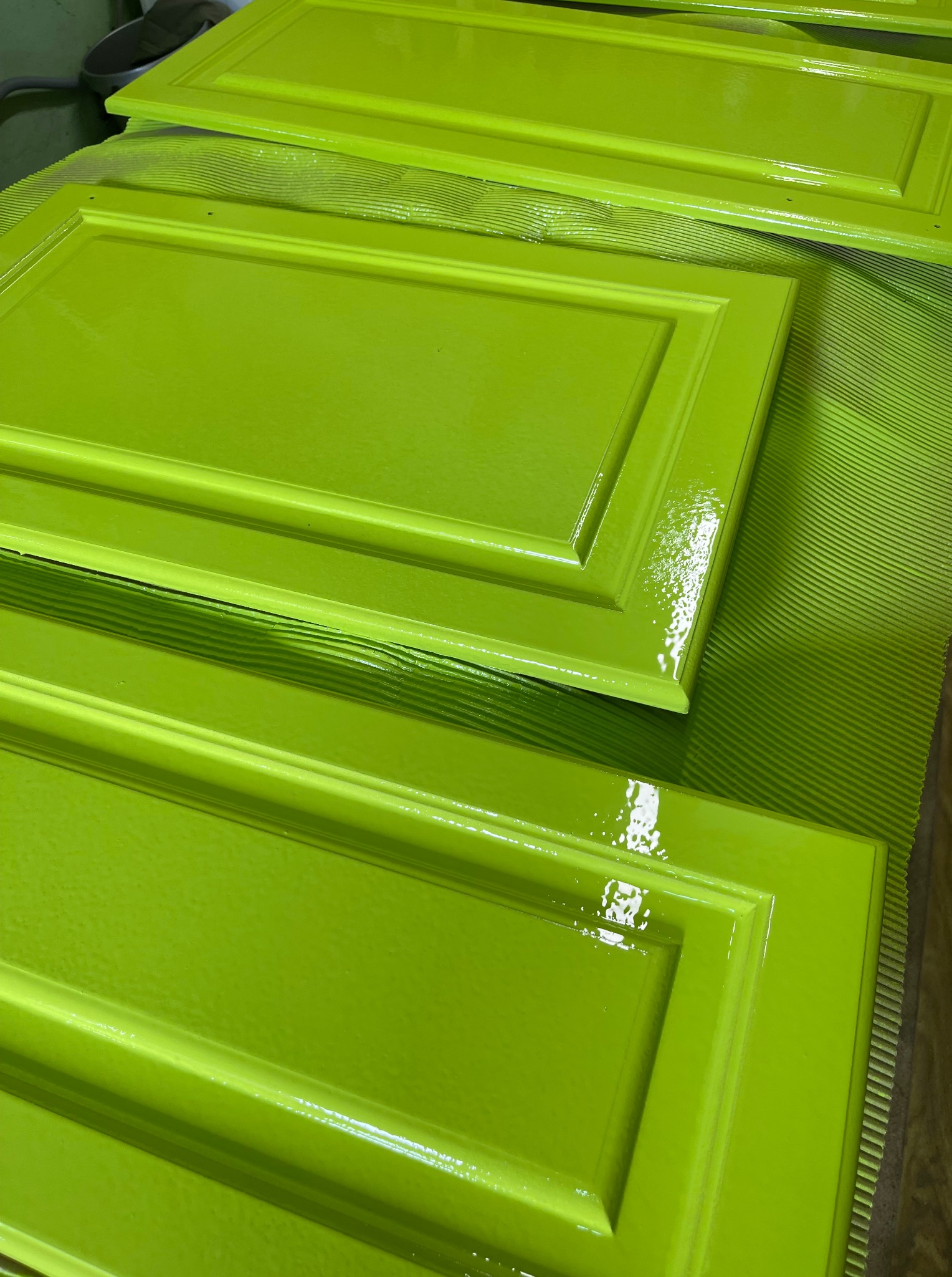 Świeżo pomalowane na jaskrawy, limonkowy kolor fronty szafek, leżące na zielonej, teksturowanej powierzchni. Widoczny połysk mokrej farby.
