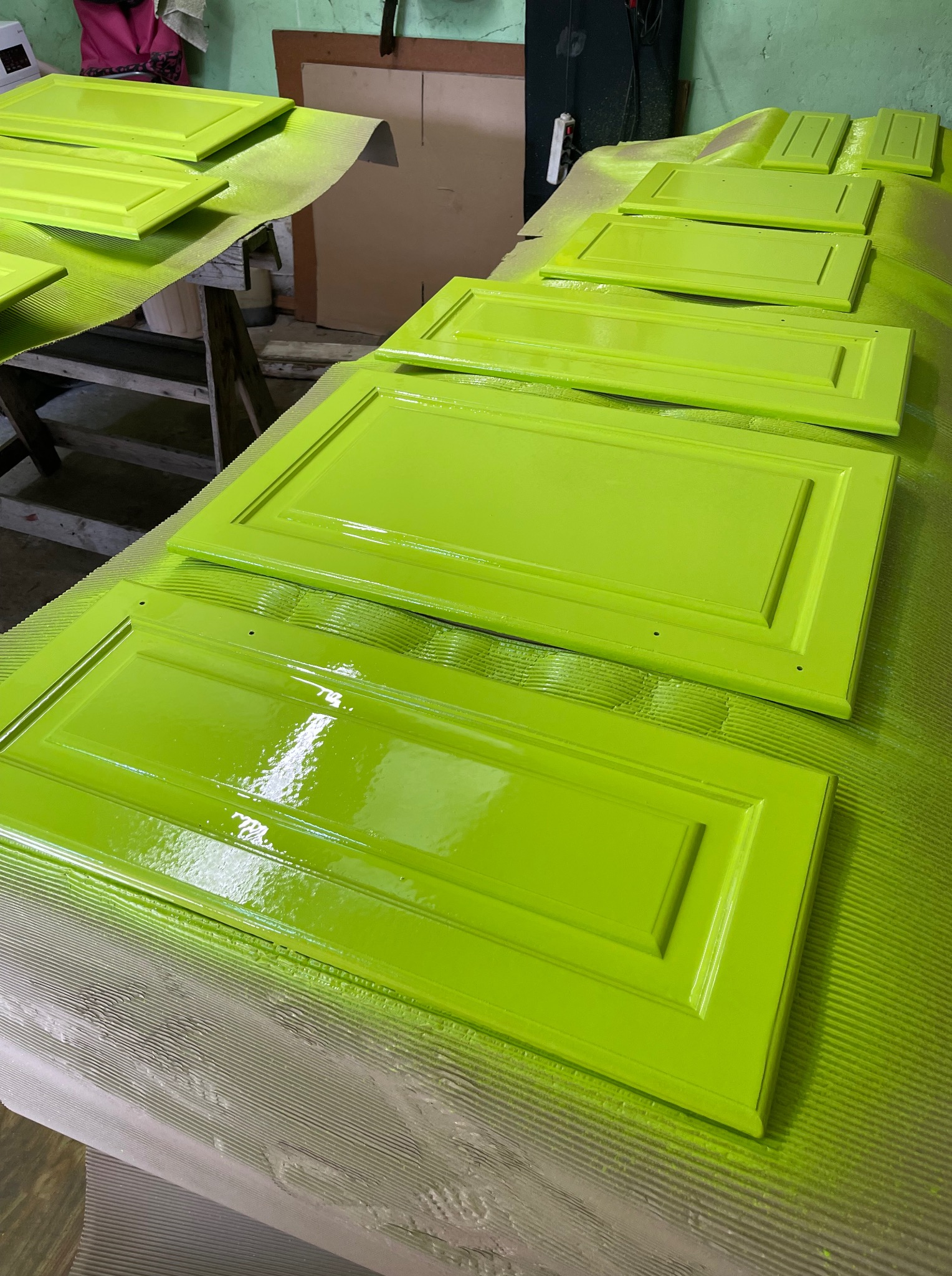 Świeżo pomalowane na jaskrawy, limonkowy kolor fronty szafek kuchennych, leżące na zabezpieczonym stole, w warsztacie. Widoczne detale wykończenia.