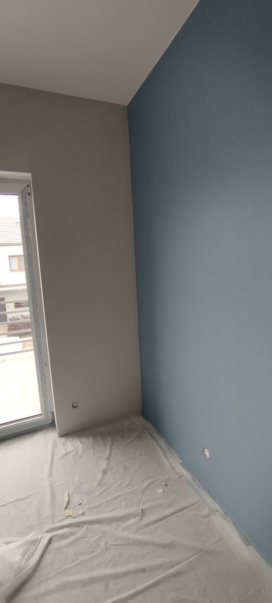 Śrem: Świeżo pomalowane ściany w pokoju na dwa odcienie szarości i błękitu. Podłoga zabezpieczona folią malarską. Widoczne gniazdka elektryczne.