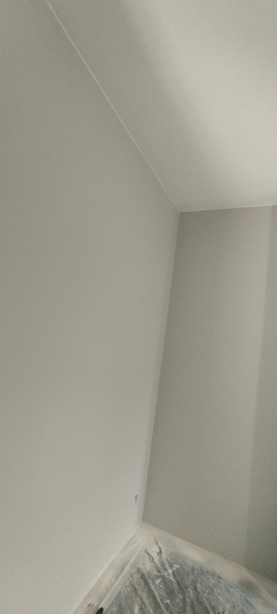Świeżo pomalowany pokój w odcieniach szarości, z widocznym zabezpieczeniem podłogi folią malarską. Minimalistyczne wykończenie ścian i sufitu, kąt ujęcia z dołu.