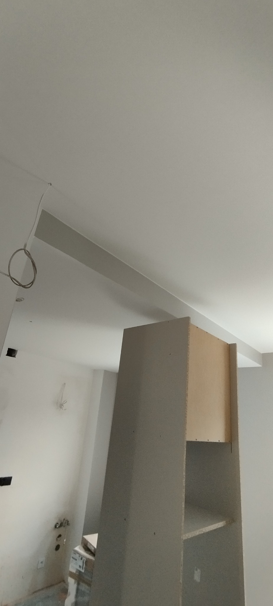 Wnętrze w trakcie prac: sufit z listwą, fragment szafy z płyty karton-gips, widoczne kable i instalacje. Ściany przygotowane do malowania.