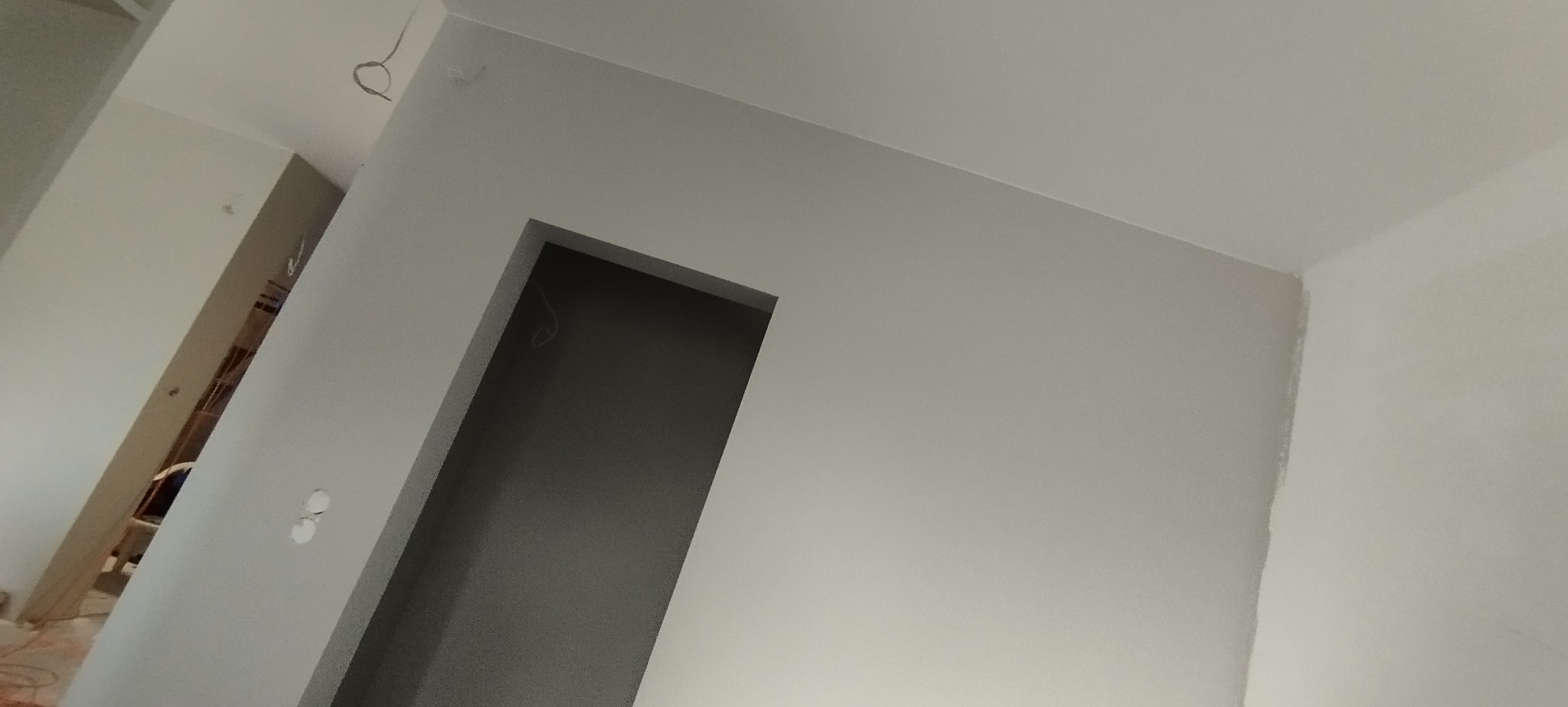 Wnętrze po malowaniu na szaro: gładkie ściany, otwór drzwiowy bez ościeżnicy, widoczne przewody elektryczne, przygotowane do dalszych prac wykończeniowych.