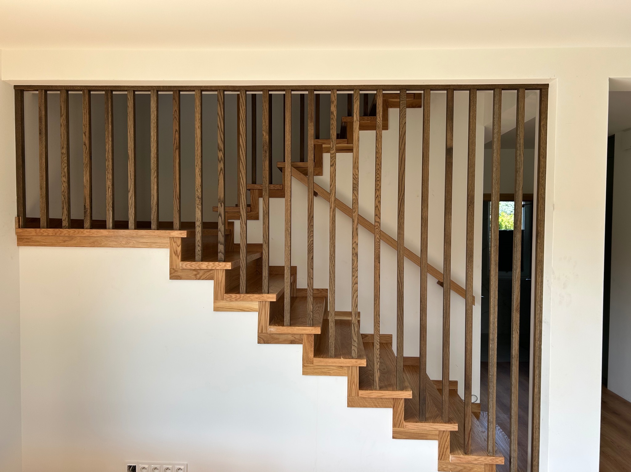 Nowoczesne schody drewniane z balustradą z pionowych listew, oświetlone naturalnym światłem. Widok z dołu, akcent na minimalistyczny design.