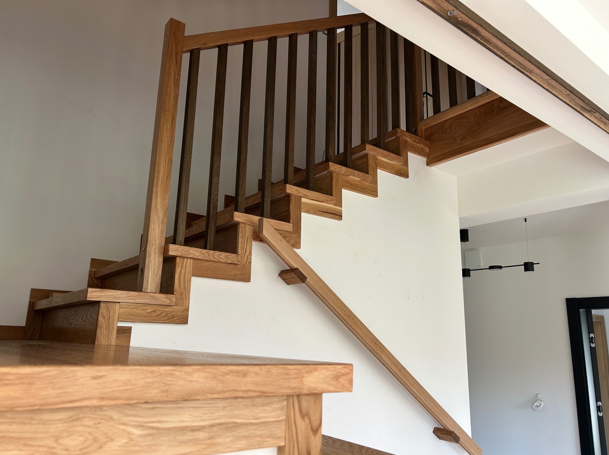 Jasne drewniane schody z ciemnymi balustradami na białej ścianie. Widok z dołu, ukazujący solidną konstrukcję i nowoczesny design.