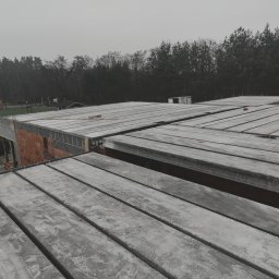 ZAKŁAD OGOLNOBUDOWLANY - Budowa domu: strop Teriva z betonowych belek i pustaków, widok z góry na szary beton i czerwoną cegłę, las w tle, pochmurny dzień.