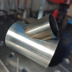 Nikstal - Precyzyjnie zespawane, nierdzewne rury pod kątem, widoczne ślady spawania. Metalowa powierzchnia z delikatnym połyskiem. Tło warsztatowe, narzędzia w tle.