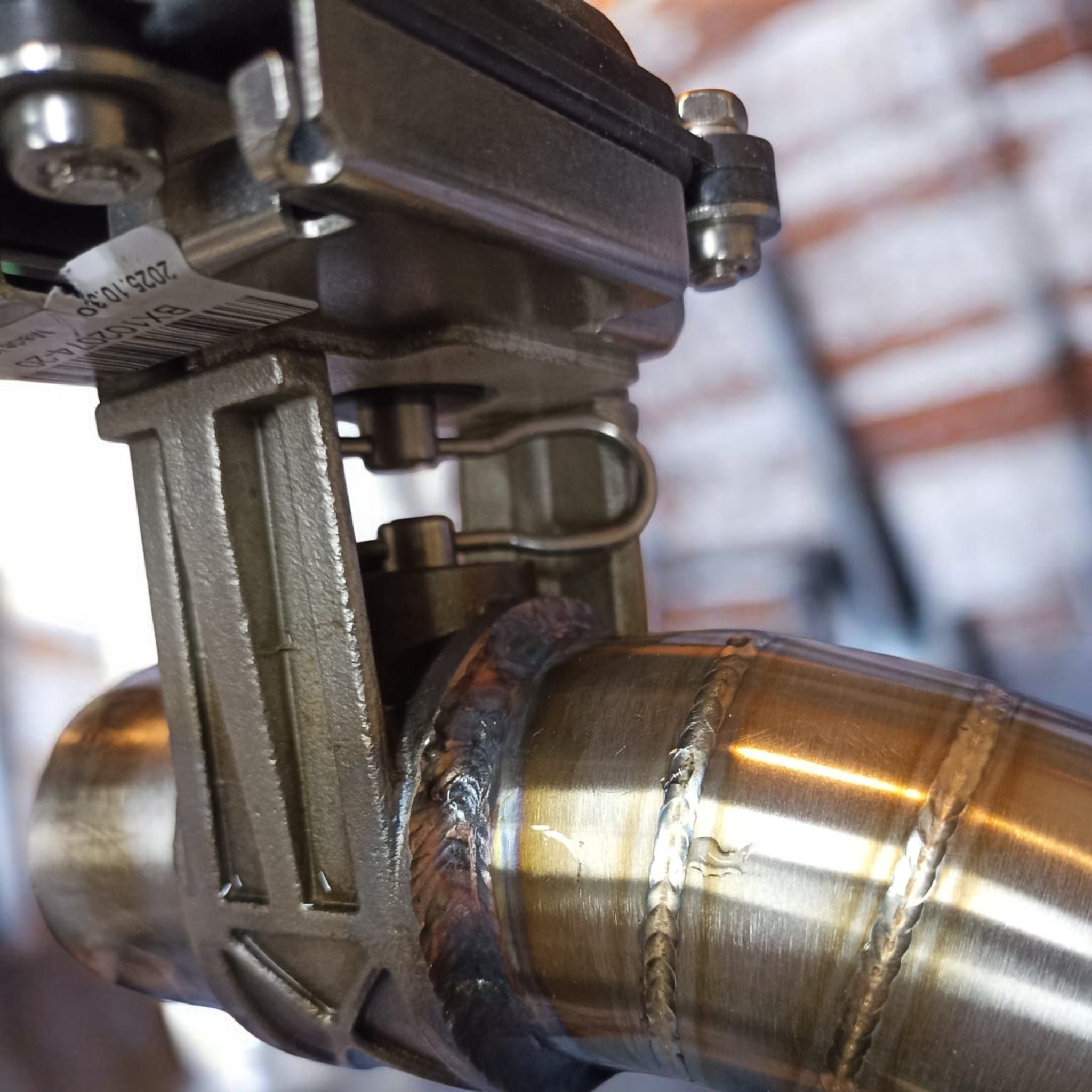 Szczegółowe zbliżenie spawu na metalowej rurze z elementami mocującymi, ukazujące precyzję i jakość wykonania. Widoczne ślady spawania i metaliczna powierzchnia.