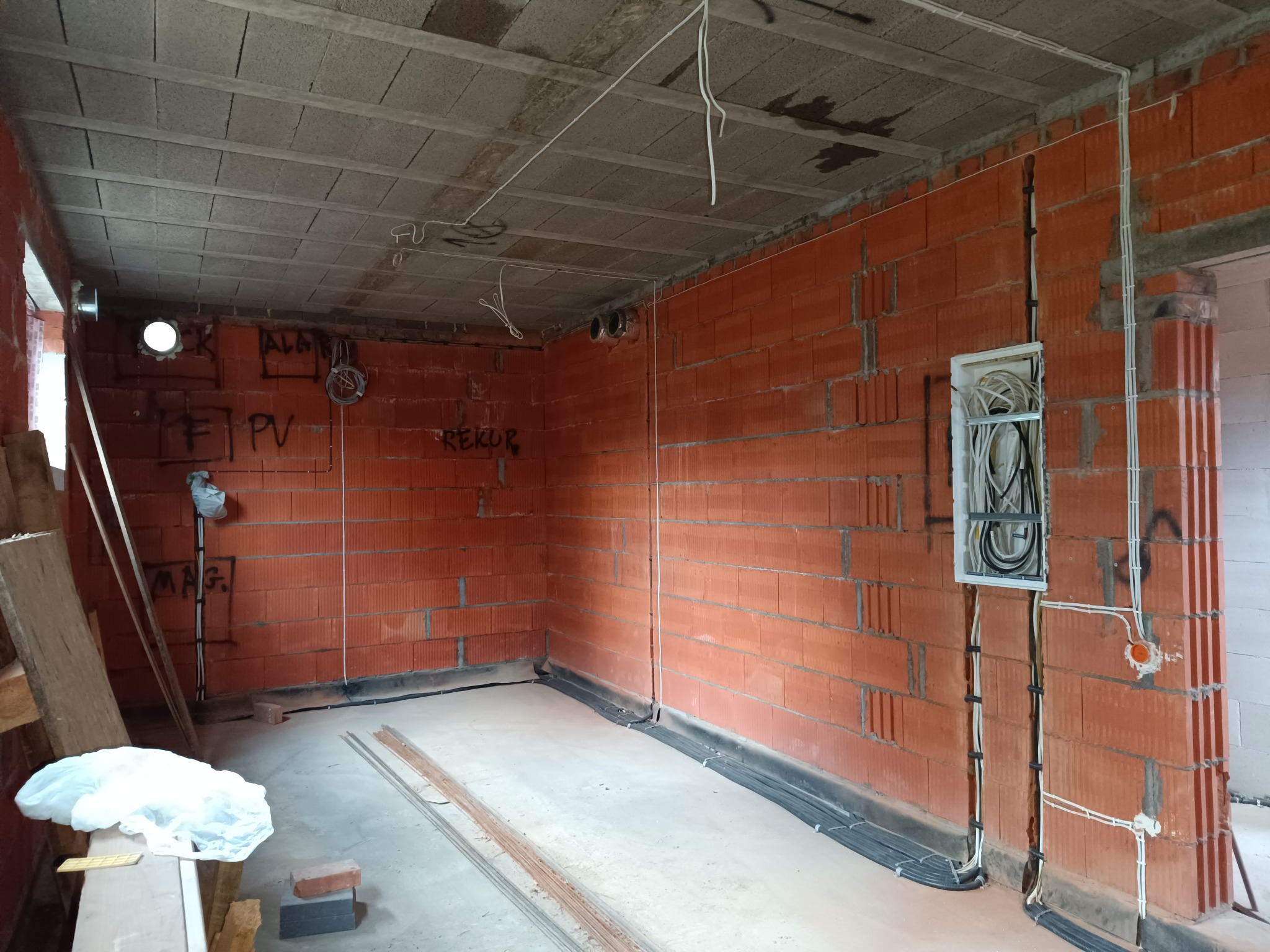 Wnętrze w trakcie prac elektrycznych: widoczne kable w ścianach z cegły, puszka elektryczna i przewody pod sufitem. Surowy stan, instalacja w trakcie realizacji.
